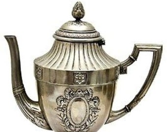 Op de afbeelding: Een zilveren theepot met een sierlijk ontwerp en een geribbeld lichaam. De theepot heeft een deksel met een knop en een tuit met een gebogen handvat.