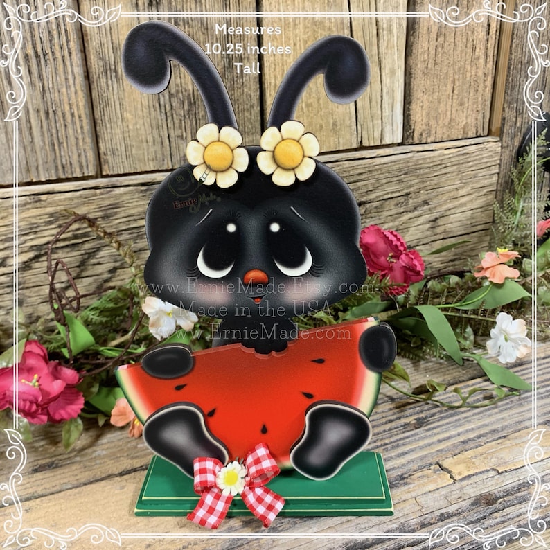 K&ouml;nnte beinhalten: Schwarz-wei&szlig;e Marienk&auml;fer mit gelben Blumen auf dem Kopf, die ein rotes Wassermelonenst&uuml;ck halten. Der Marienk&auml;fer sitzt auf einem gr&uuml;nen Sockel mit einer rot-wei&szlig; karierten Schleife. Misst 10,25 Zoll hoch.