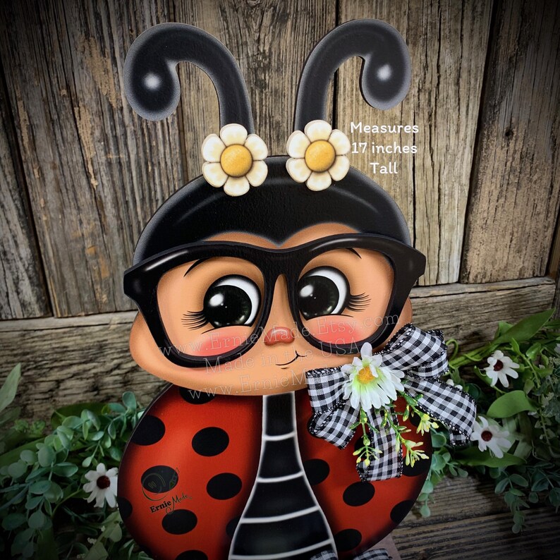 May include: A hand-painted wooden ladybug with black glasses, red and black polka dots, and a white daisy with a black and white checkered bow. The ladybug is 17 inches tall. Measures 17 inches Tall.