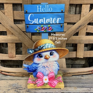 May include: A blue and white bird figurine wearing a straw hat with a blue gingham ribbon. The figurine is on a yellow base with a pink bow and daisy. A blue sign above reads "Hello Summer". Measures 17 1/2 inches tall.