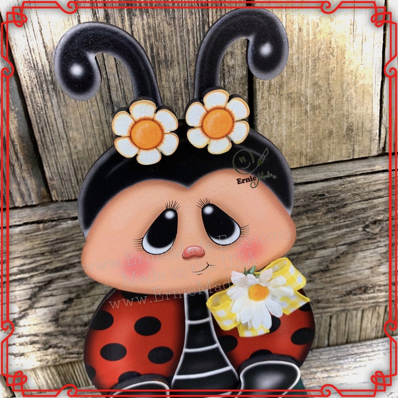 May include: A hand-painted wooden ladybug figurine with black spots, red wings, and a white daisy flower. The ladybug has a black head with two white flowers with yellow centres. The ladybug has large, black eyes and a sweet expression. The figurine is made in the USA.