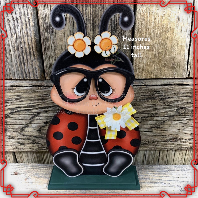 May include: A wooden ladybug figurine with black glasses, red and black polka dot wings, and a yellow daisy with a yellow bow. The ladybug is sitting on a green base. Measures 11 inches tall.