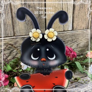 K&ouml;nnte beinhalten: Ein schwarzer Marienk&auml;fer mit wei&szlig;en Punkten und gelben Blumen auf dem Kopf h&auml;lt ein St&uuml;ck Wassermelone. Der Marienk&auml;fer ist 26 cm gro&szlig;. Der Marienk&auml;fer ist auf Holz gemalt und hat einen verspielten, cartoonartigen Stil.