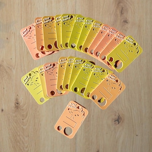 May include: A collection of rectangular tags in shades of yellow and orange, each featuring a cutout of a fox head, the text "STAY CRAFTY," two circular holes at the bottom, and a small hole at the top for hanging, arranged in a fan-like pattern.