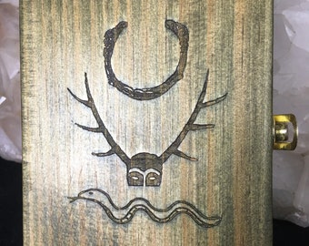 Può includere: Una scatola di legno con un design intagliato di una luna crescente, corna e un serpente. La scatola è macchiata in tonalità di verde e marrone.