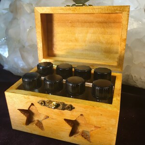 May include: A wooden box with a star-shaped cutout design, containing small glass bottles with black caps. The box has a brass latch and is open, revealing the bottles inside.