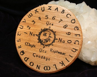 May include: A round, wooden Ouija board with engraved letters, numbers, and phrases. The board features a sun and moon design in the center. The letters and numbers are arranged around the edge of the board.