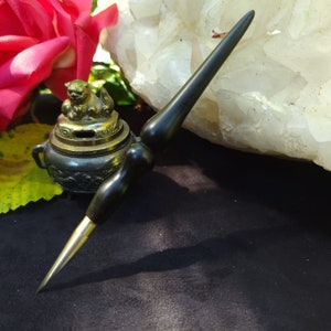 May include: A black wooden incense stick holder with a gold metal incense burner. The incense burner features a small, detailed animal figurine on top. The holder and burner are sitting on a dark surface.