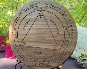 May include: A round, wooden plaque with engraved text and symbols. The plaque features a central triangle and circular text that reads "ORIGNS", "TETRA", "GRAMMA", "NOL", and "PAYMON". The plaque is displayed on a black metal stand.