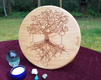 May include: A round wooden board featuring a laser-etched design of a tree of life with detailed roots and branches. The tree is encircled by a geometric pattern of circles and lines.