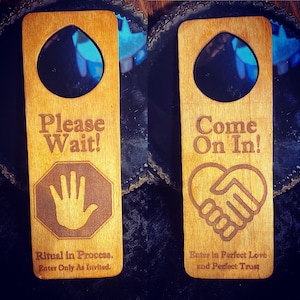 May include: Two wooden door hangers with a natural finish. One reads "Please Wait!" with a hand symbol and "Ritual in Process. Enter Only As Invited." The other says "Come On In!" with a handshake and heart symbol and "Enter in Perfect Love and Perfect Trust."