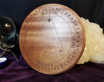 May include: A wooden circle with a triangle inscribed inside. The triangle has a cross at the top and two stars at the bottom. The circle is surrounded by a ring of text that includes the names "Michael", "Gabriel", "Uriel", and "Raphael".