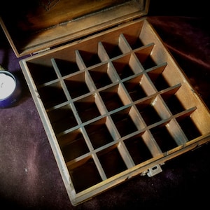 May include: A wooden box with a hinged lid and a compartmentalized interior. The box is made of dark wood and has a natural finish. The compartments are arranged in a grid pattern and are empty.