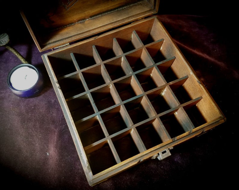 May include: A wooden box with a hinged lid and a compartmentalized interior. The box is made of dark wood and has a natural finish. The compartments are arranged in a grid pattern and are empty.