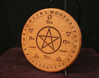 May include: A round wooden Ouija board with engraved letters, numbers, and symbols. The board features a central pentagram and the words "Yes," "No," and "Maybe." The letters of the alphabet are arranged around the edge.