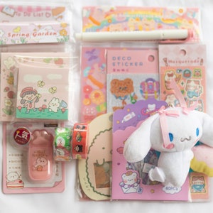 May include: A collection of stationery items, including stickers, notepads, and decorative tape, in shades of pink and pastel colors. A plush white bunny with a pink bow is also included. The items feature cute illustrations and the text "To Do List" and "Spring Garden".