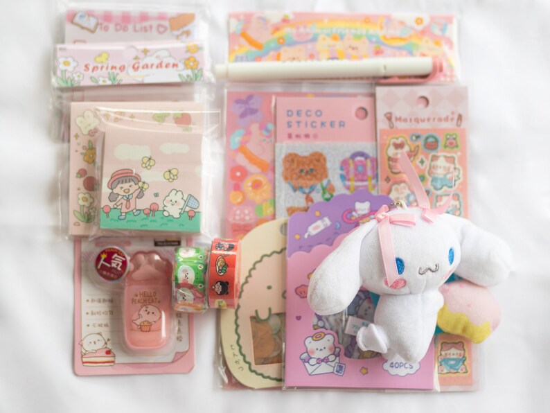 May include: A collection of stationery items, including stickers, notepads, and decorative tape, in shades of pink and pastel colors. A plush white bunny with a pink bow is also included. The items feature cute illustrations and the text "To Do List" and "Spring Garden".