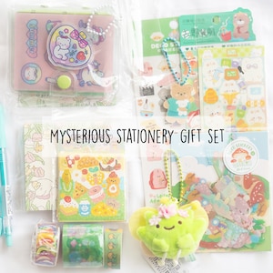 May include: A collection of stationery items, including stickers, a pen, a small notebook, and decorative tape, all packaged in clear plastic. The items feature cute illustrations of bears, food, and flowers. The text "MYSTERIOUS STATIONERY GIFT SET" is displayed.