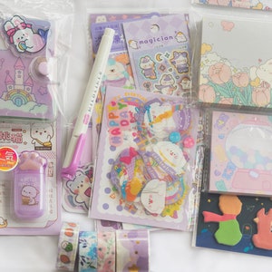May include: An assortment of stationery items in pastel colors. Includes a purple notebook, stickers, washi tape, a pen, and memo pads. The items feature cute illustrations of animals, castles, and other whimsical designs.