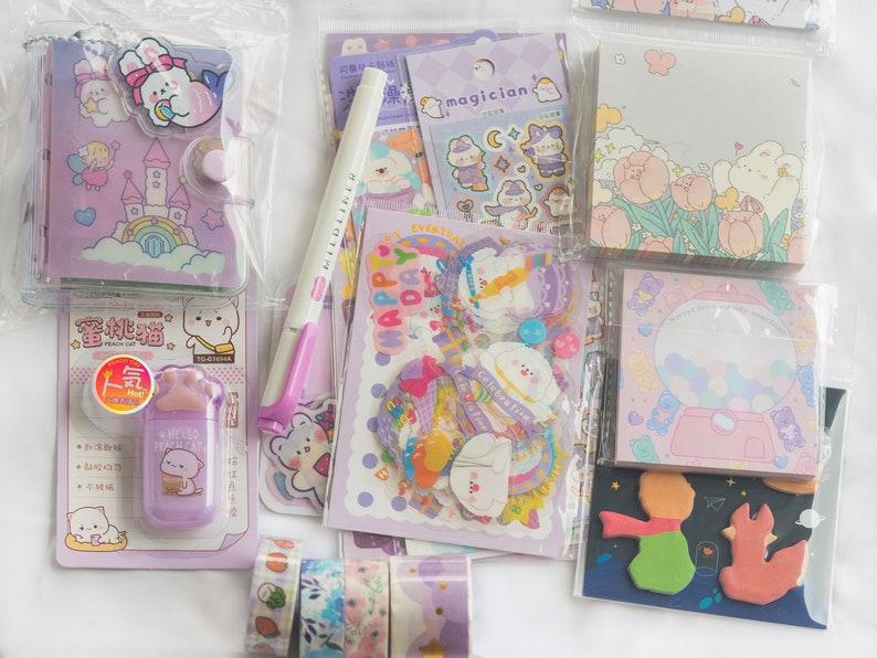 May include: An assortment of stationery items in pastel colors. Includes a purple notebook, stickers, washi tape, a pen, and memo pads. The items feature cute illustrations of animals, castles, and other whimsical designs.