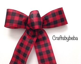 May include: A red and black buffalo plaid ribbon bow. The bow is tied with a double loop and the ends are cut into a point. The text "Craftsbybeba" is visible in the lower right corner of the image.