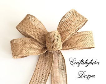 May include: A large, brown burlap bow with a long, pointed tail. The bow is tied in a classic, symmetrical style. The bow is made of a coarse, woven fabric with a natural, rustic look.
