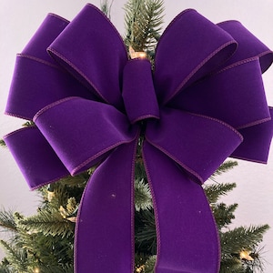 May include: A large purple velvet bow with a wired edge, perfect for a Christmas tree topper. The bow is tied with a double loop and has long tails.