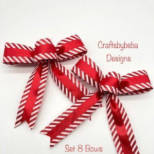 May include: A set of eight red and white striped bows with a glittery finish. The bows are tied with a satin ribbon and are perfect for adding a festive touch to any occasion.  "Craftsbybeba Designs" is written in the top right corner of the image.  "Set 8 Bows" is written in the bottom centre of the image.