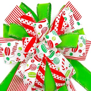 May include: A Christmas bow made with red and white striped ribbon, green ribbon with glitter, and white ribbon with a candy cane and lollipop pattern. The bow is tied in a large, full shape.