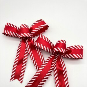 May include: Two red and white striped bows with a satin finish. The bows are tied together and are ready to be used for decorating.