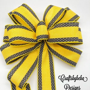 May include: A large yellow and black striped bow with white polka dots. The bow is made of two different ribbons, one with black stripes and one with white polka dots. The bow is tied with a loop and a tail. The bow is perfect for decorating a wreath or a gift.