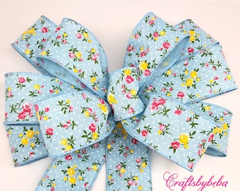 May include: A large blue bow with a white polka dot pattern and a floral print featuring pink, yellow, and green flowers. The bow is tied with a long tail and is perfect for adding a touch of elegance to any occasion.