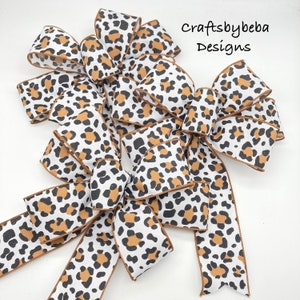 May include: A set of three leopard print bows, made with brown and white ribbon. The bows are tied together and arranged in a decorative fashion. The text "craftsbybeba Designs" is visible in the top right corner of the image.