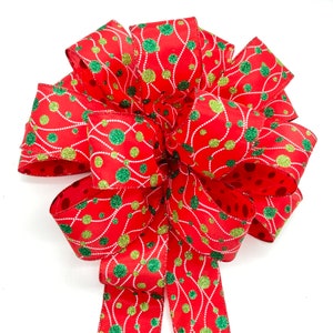 May include: A red, green, and gold Christmas bow with a polka dot pattern. The bow is made of ribbon with a shiny, glittery finish.