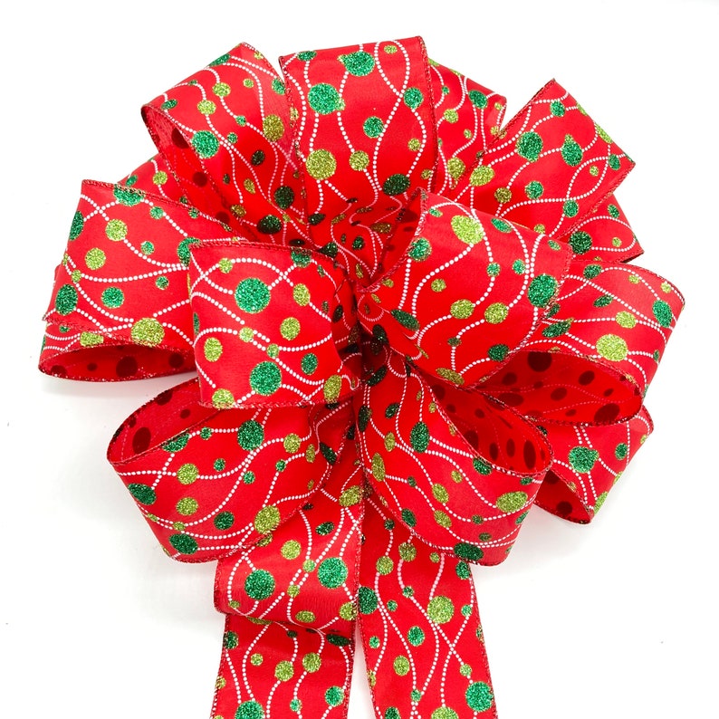 May include: A red, green, and gold Christmas bow with a polka dot pattern. The bow is made of ribbon with a shiny, glittery finish.