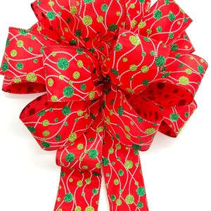 May include: A red, green, and gold Christmas bow with a polka dot pattern. The bow is made of ribbon with a glittery finish.