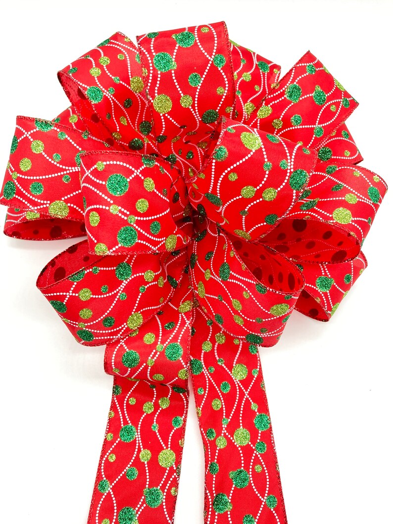 May include: A red, green, and gold Christmas bow with a polka dot pattern. The bow is made of ribbon with a glittery finish.