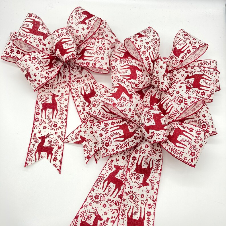 May include: Two large red and white bows with a deer and floral pattern. The bows are made of a soft, textured fabric and are perfect for adding a touch of holiday cheer to any space.