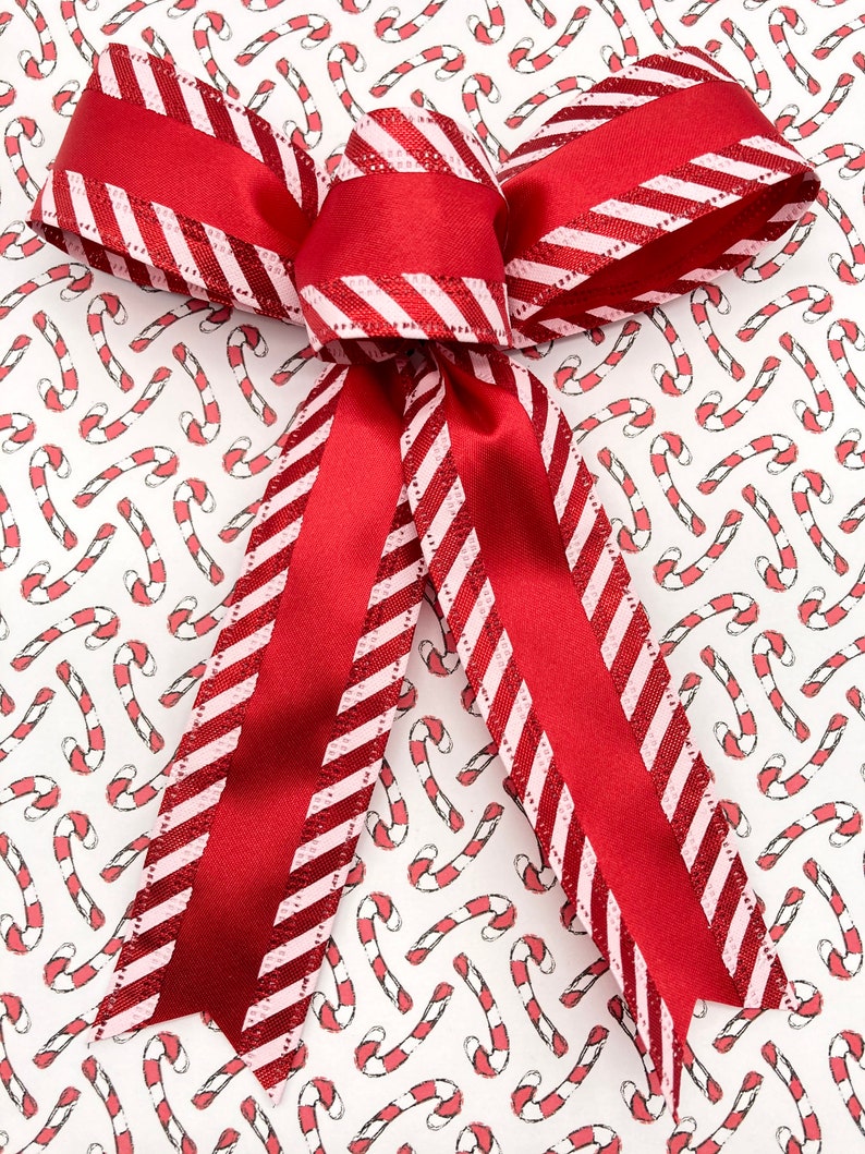 May include: A red and white striped ribbon bow tied on a white background with a repeating pattern of red and white candy canes.
