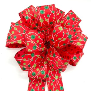 May include: A red, green, and gold Christmas bow with a polka dot pattern and a white string design. The bow is made of ribbon and is tied in a knot.