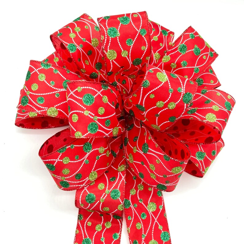May include: A red, green, and gold Christmas bow with a polka dot pattern and a white string design. The bow is made of ribbon and is tied in a knot.