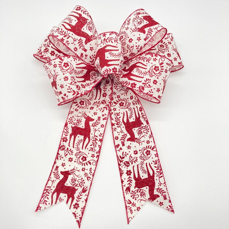 May include: A red and white Christmas bow with a reindeer and floral pattern. The bow is tied with a long tail.