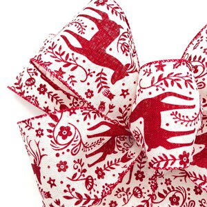 May include: Red and white patterned ribbon with a design of stylized deer, flowers, and leaves. The ribbon is folded into a bow shape.