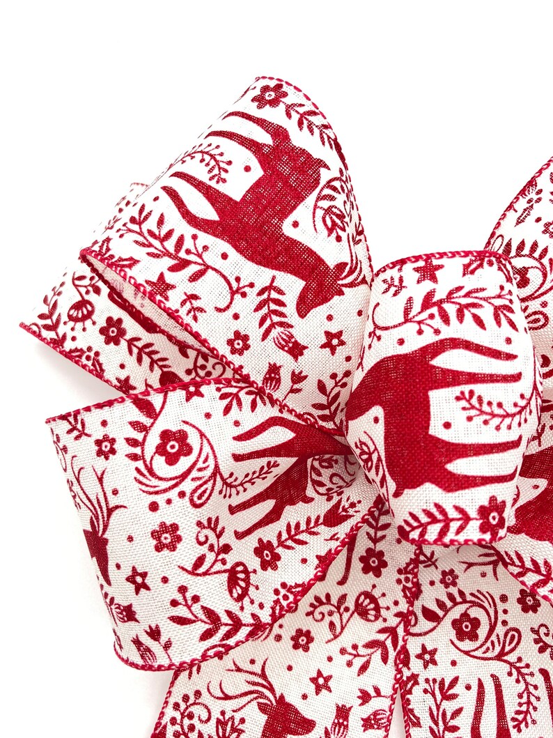 May include: Red and white patterned ribbon with a design of stylized deer, flowers, and leaves. The ribbon is folded into a bow shape.