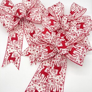 May include: Two large red and white Christmas bows with a deer and floral pattern. The bows are made of wired ribbon and are ready to be tied on a wreath or gift.
