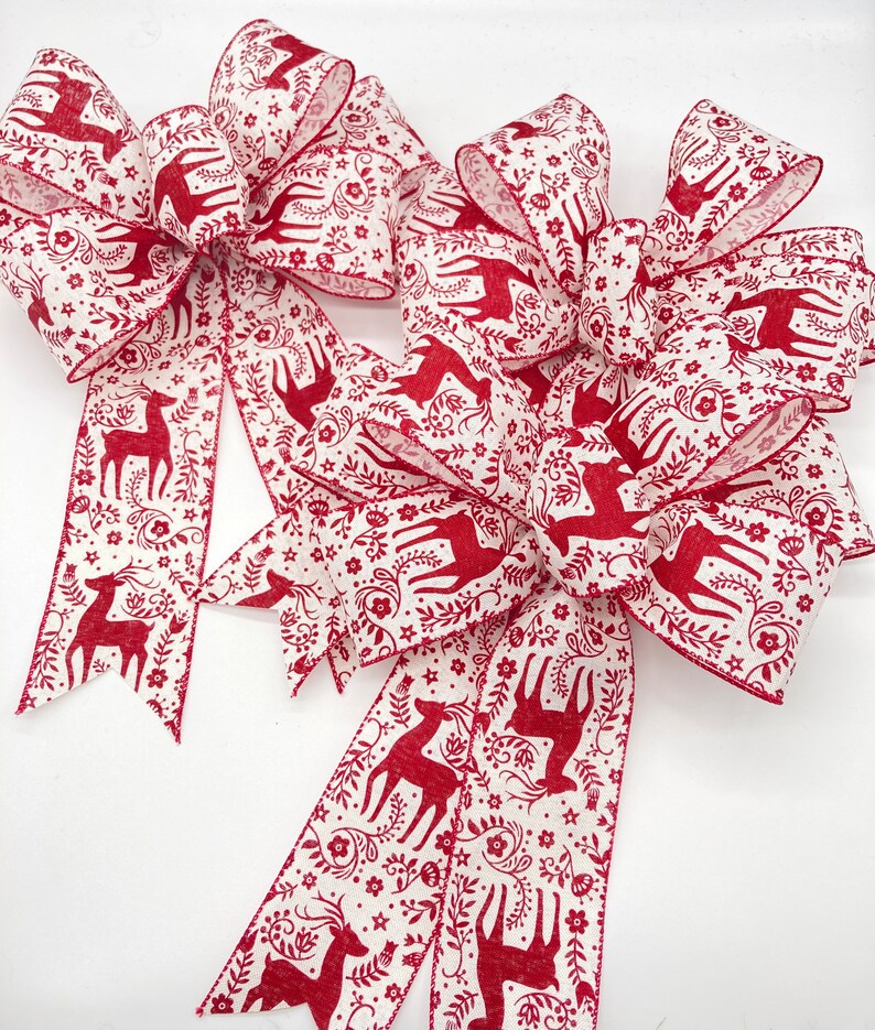 May include: Two large red and white Christmas bows with a deer and floral pattern. The bows are made of wired ribbon and are ready to be tied on a wreath or gift.