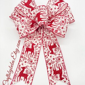 May include: A red and white Christmas bow with a reindeer and floral pattern. The bow is tied with a double loop and two tails.
