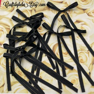 May include: A group of black satin ribbon bows with gold trim. The bows are tied with long tails and are arranged on a background of yellow roses.