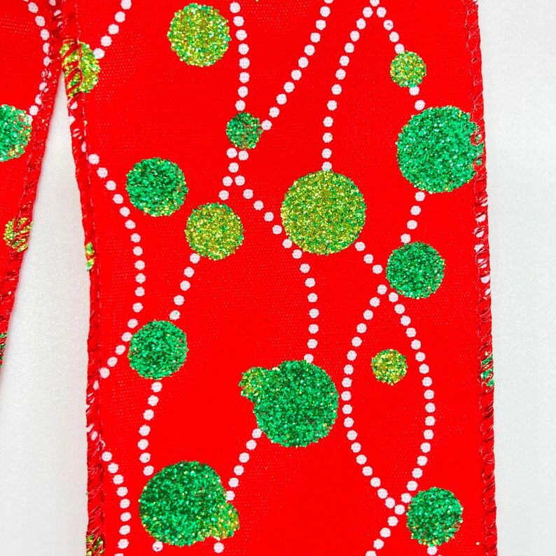 May include: Red ribbon with a white and green polka dot pattern. The dots are green with a glittery finish and are arranged in a random pattern on the ribbon.