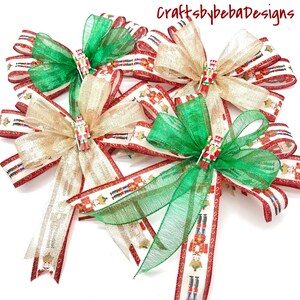 May include: Several decorative bows with green and gold sheer ribbons, and a red and white patterned ribbon featuring toy soldiers. Each bow has a small toy soldier embellishment in the center. The text "CraftsbybebaDesigns" is in the upper right corner.